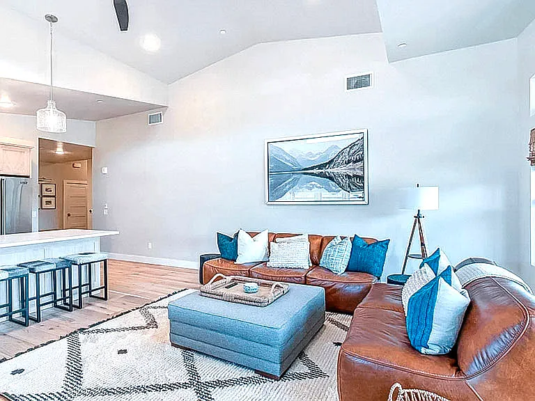 Open-concept living and dining area with leather sofa, mountain artwork, hardwood floors, and kitchen island with bar seating