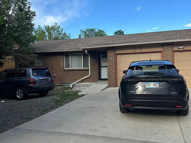 Single-story brick home with an attached garage, concrete driveway, and front entry walkway framed by mature trees.
