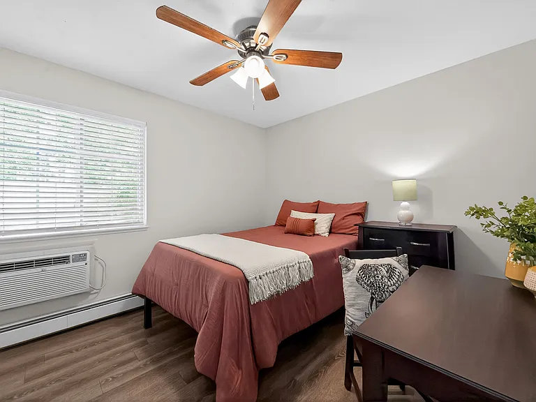 Cozy bedroom with a wooden floor, featuring a comfortable double bed, ceiling fan, and chic decor. Cozy bedroom with a wooden floor, featuring a comfortable double bed, ceiling fan, and chic decor.