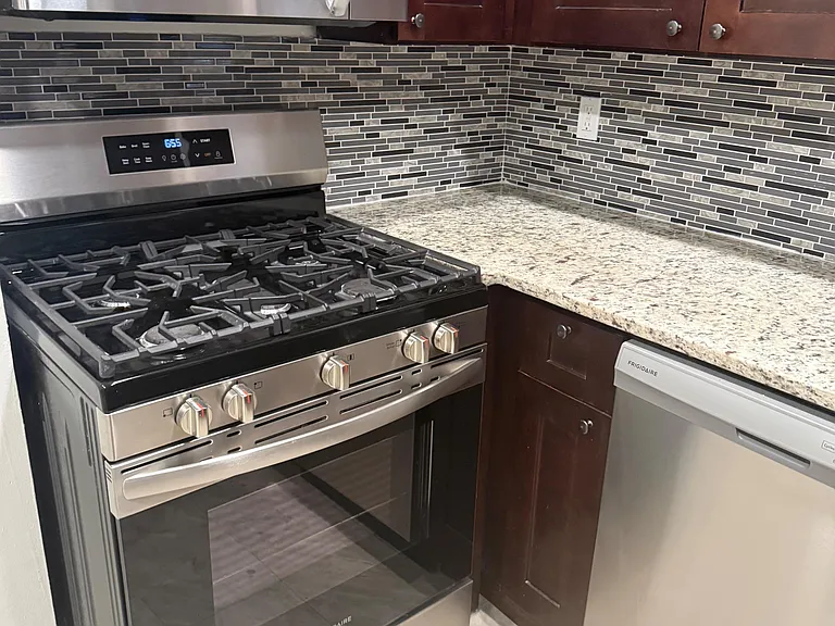 Kitchen features stainless steel gas range and microwave, granite-look counters, and a tiled backsplash with ample cabinetry.