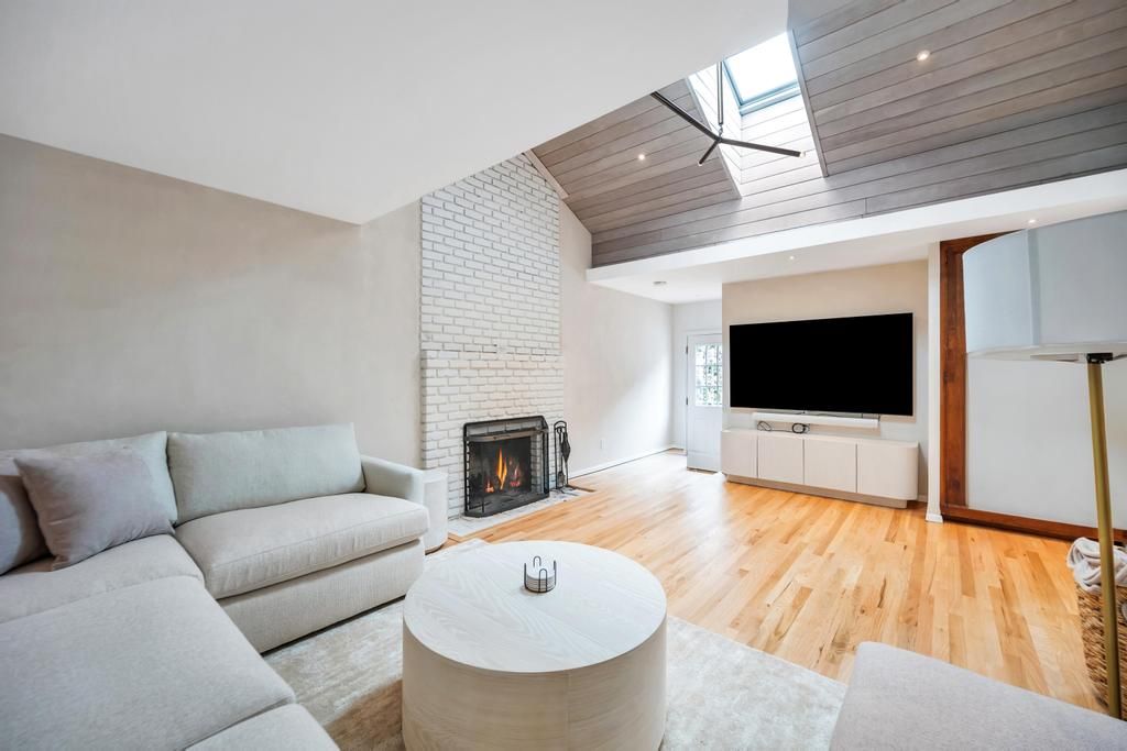  Spacious Living room with high ceilings, skylights, large couch, tv, and fireplace.