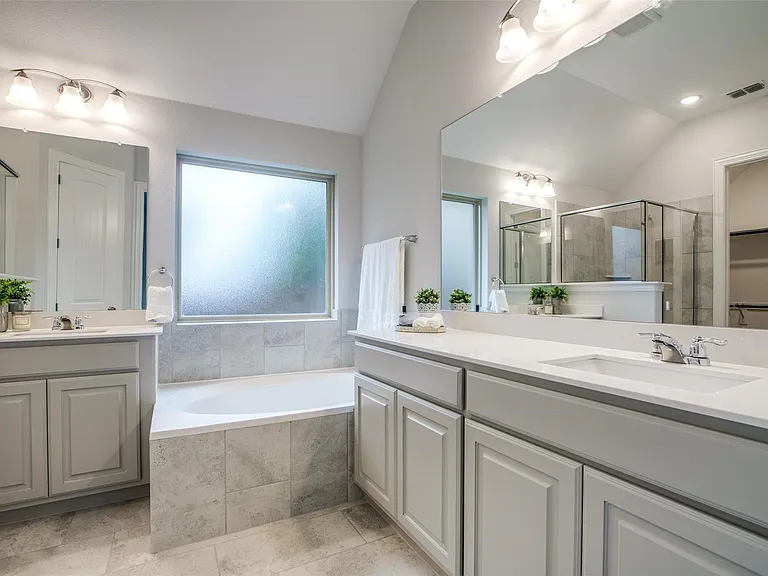 Bathroom featuring a built-in tub, dual vanities with integrated sinks, and ample overhead lighting