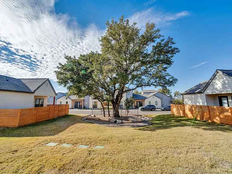 A tree stands in the middle of a grassy area between two houses.