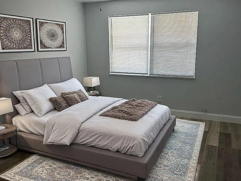 Cozy bedroom featuring a plush bed with soft pillows, elegant artwork, and natural light filtering through blinds.