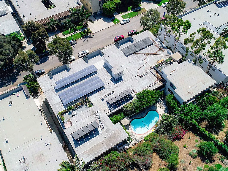 Aerial drone view of Rose North Apartments showing solar panels, energy efficient roof, and courtyard with pool.