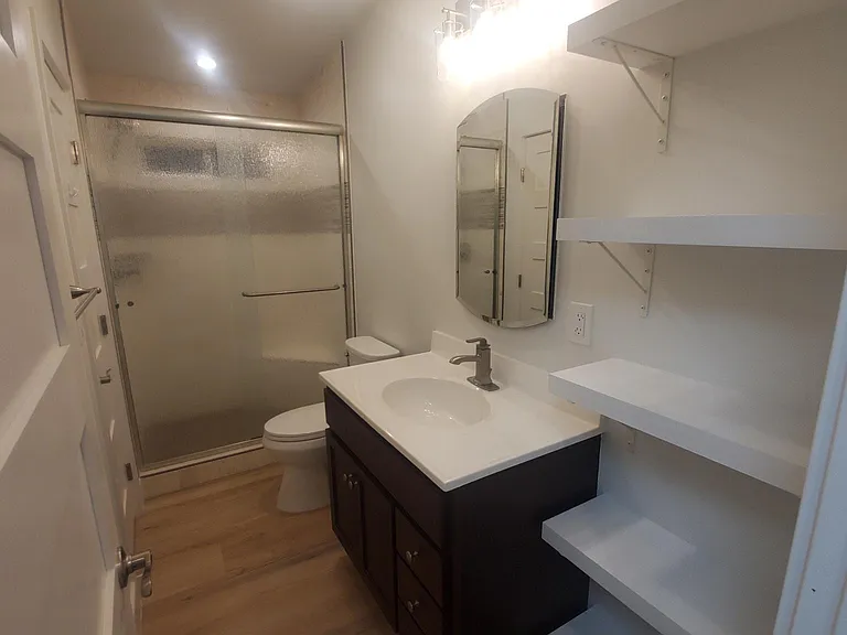 Bathroom #1 with new shelves, mirrored medicine cabinet, sink, vanity, lights, toilet, shower tile and doors.