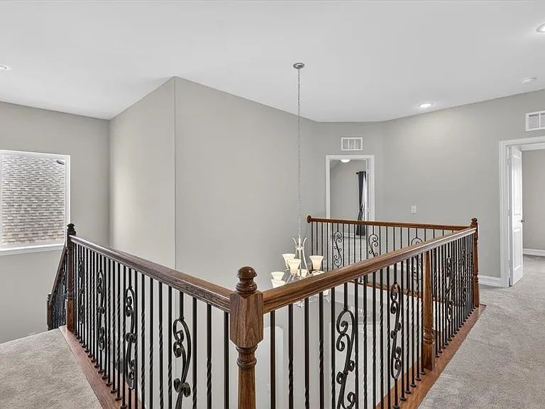 Upper-level landing featuring wrought iron balusters with a wood handrail, recessed lighting, and neutral carpeting