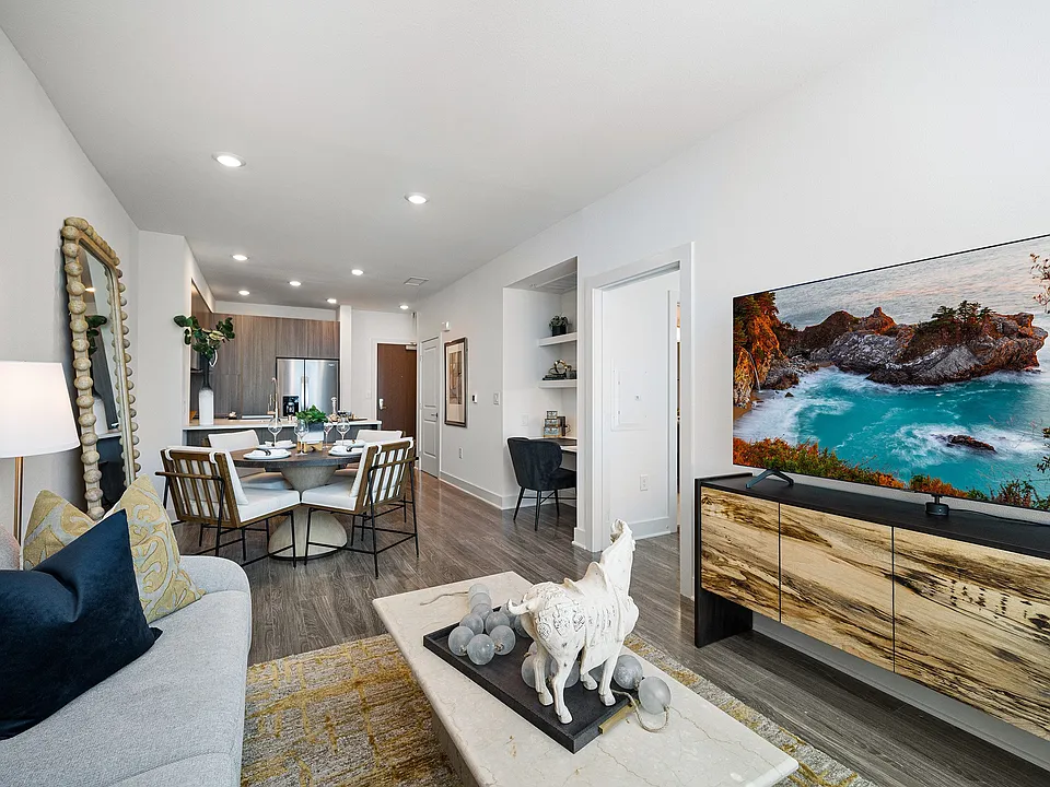 Bright living room with furnishings, wall-mounted TV, and dining