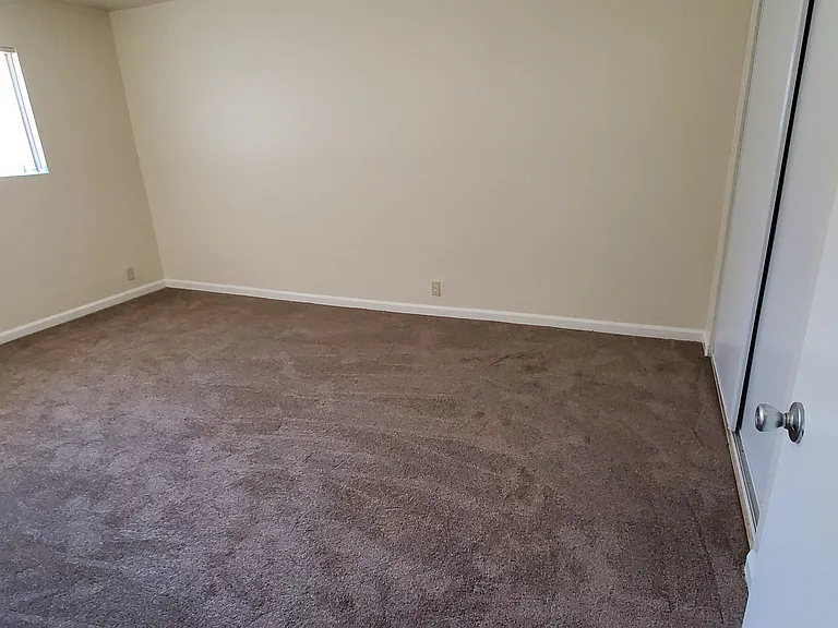 Carpeted bedroom with lots of natural light and large closets at Zenith Place Apartments in Chula Vista, California.