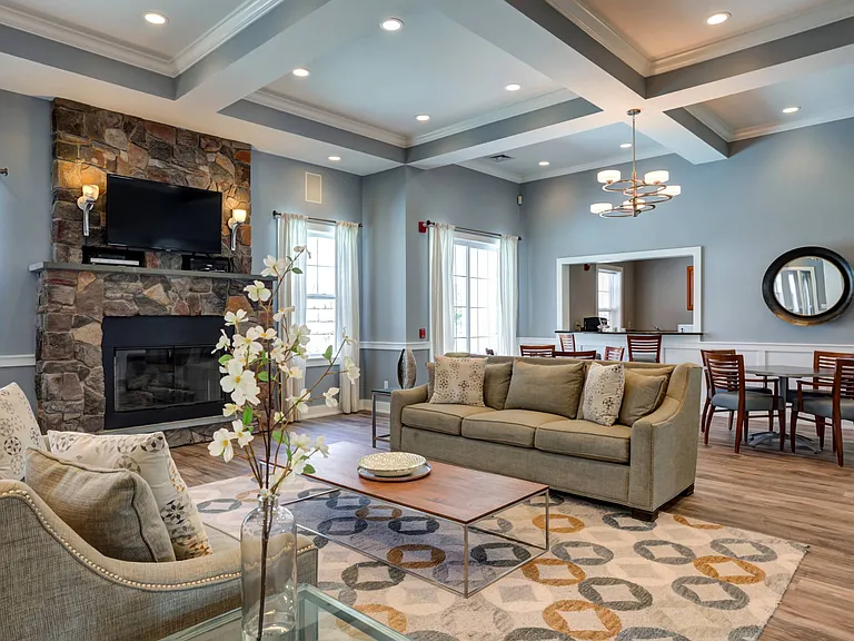 Angled view of furnished clubhouse with couches situated in front of fireplace and two tables with four chairs in background at Summit Place apartments in Methuen, MA.