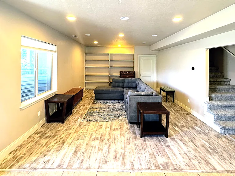 Family room with built in shelves for books, games, decor, blankets. Includes sectional sofa, two side tables, TV stand, TV.
