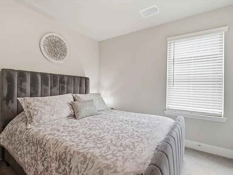 Secondary bedroom with neutral tone wall paint with white trim, carpeting, and a window with blinds.