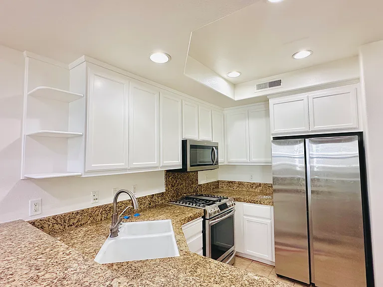 Kitchen equipped with sparkling granite countertops, an elegant tile backsplash, brand-new refrigerator, premium stainless steel appliances, and a high-end Samsung gas stove.