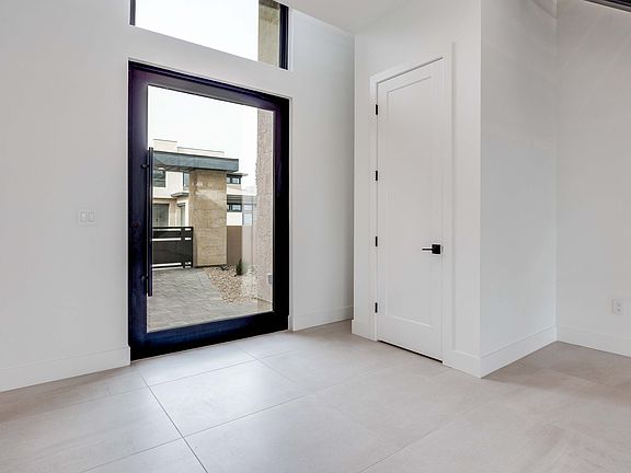 A spacious, minimalist interior with a large window, a white door, and a tiled floor, creating a bri