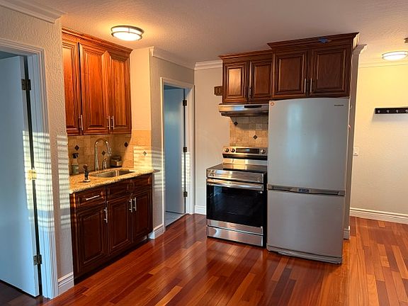 Kitchenette with new Samsung induction stovetop and oven. Existing Samsung refrigerator with icemaker (Fridge = top, Freezer = bottom), kitchen sink with pull-down faucet and garbage disposal. Range hood to ventilate stovetop.