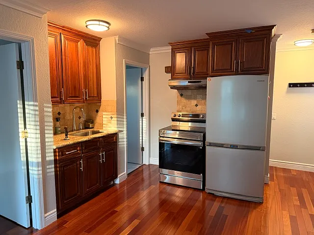 Kitchenette with new Samsung induction stovetop and oven. Existing Samsung refrigerator with icemaker (Fridge = top, Freezer = bottom), kitchen sink with pull-down faucet and garbage disposal. Range hood to ventilate stovetop.