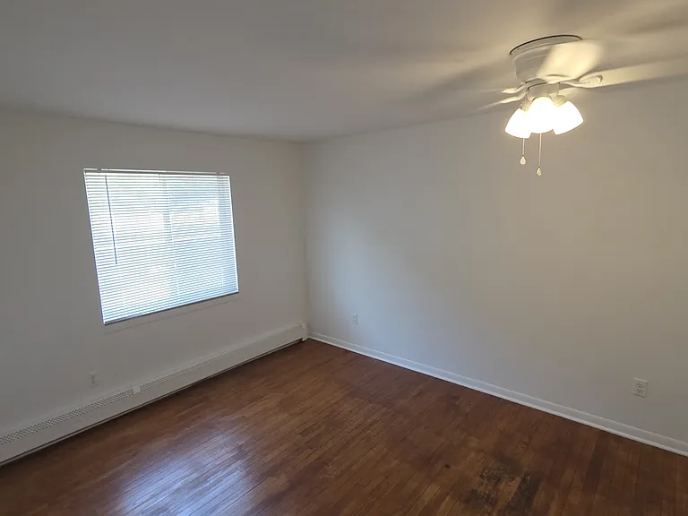 Bright second bedroom with hardwood flooring, ceiling fan, and natural light.