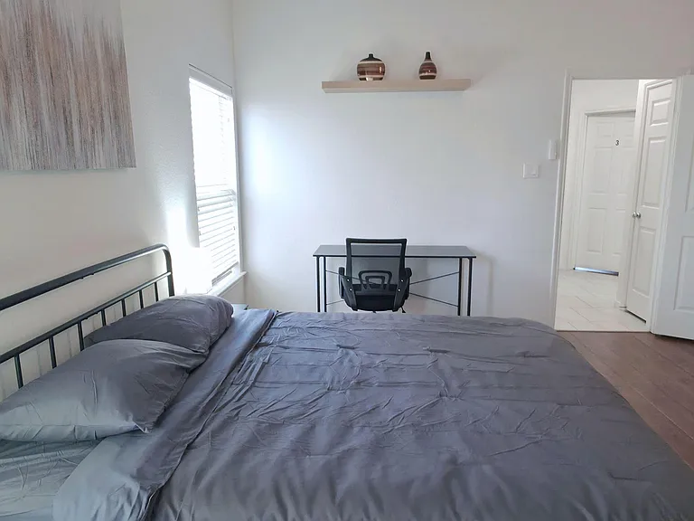 Private bedroom with a furnished bed, work desk, and window with blinds, plus easy access to the hallway.