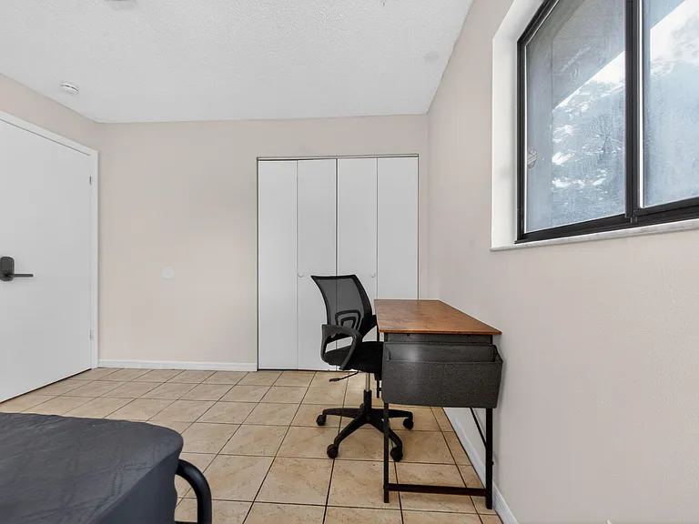 Bedroom with tile flooring, a large window, and a closet plus a dedicated desk area for work or study.