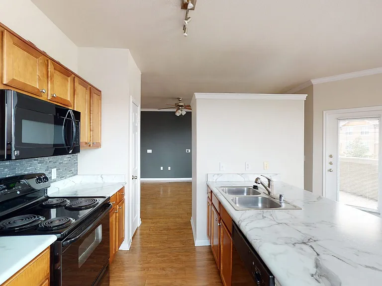 Apartment kitchen with marble-style countertops and wood-style flooring.