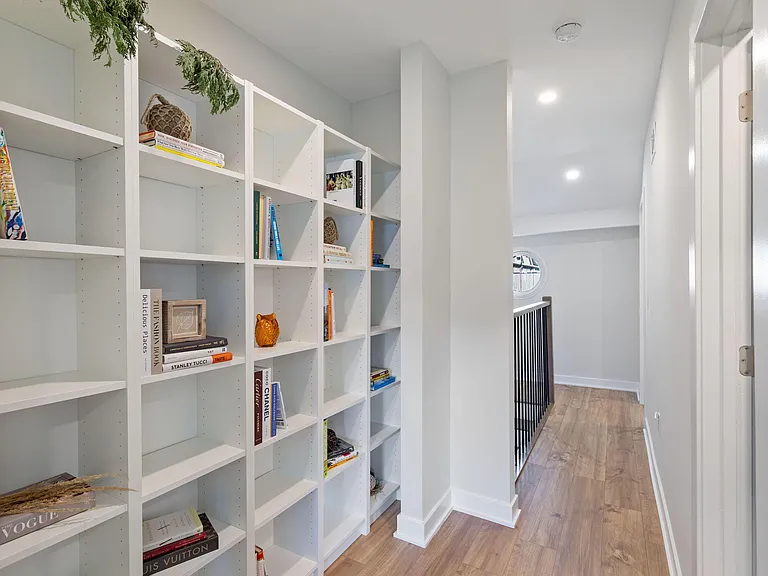 Upper-level hallway with built-in shelving for books and decor, plus wood-look flooring and recessed lighting.