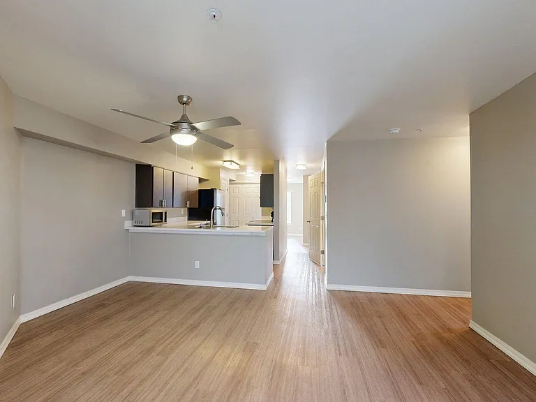 Apartment kitchen with stainless steel appliances, dining and living room with wood-style flooring.