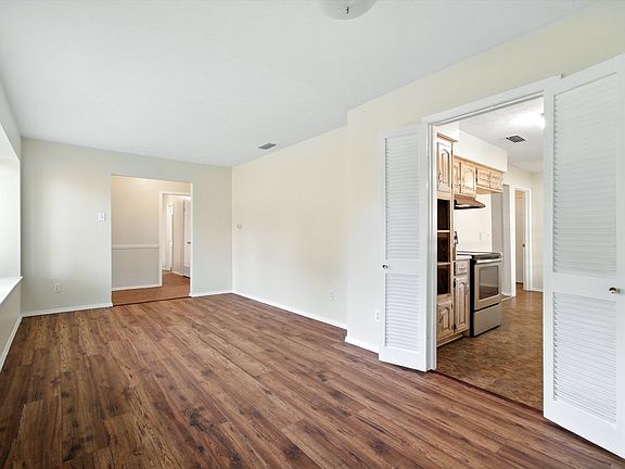 Spacious combined formal dining and living room with sightline to kitchen entrance and large front windows showcasing landscaped yard.