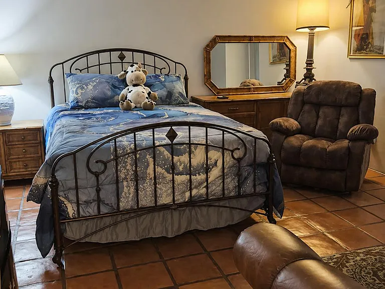 Furnished bedroom with a metal bed frame, nightstand, dresser with mirror, and seating on durable tile flooring.