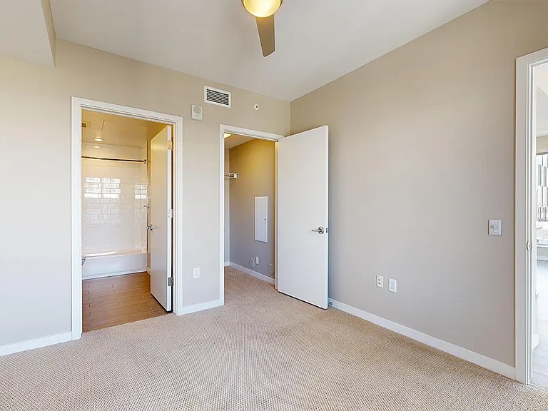 Spacious apartment bedroom with large closet, attached bathroom and plush carpet flooring.