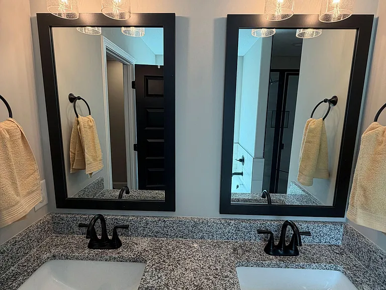Double-sink vanity with granite-look counters, matte-black fixtures, and framed mirrors plus updated wall lighting.
