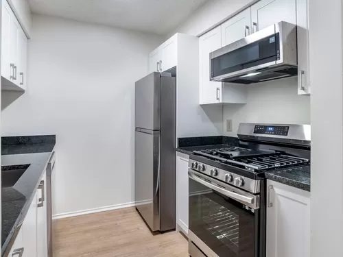Renovated Package II kitchen with stainless steel appliances, granite countertops, white cabinetry, and hard surface flooring - eaves Fair Lakes