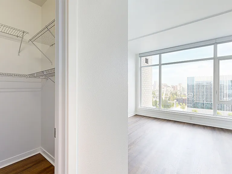 Spacious apartment bedroom with large closet, attached bathroom and wood-style flooring.