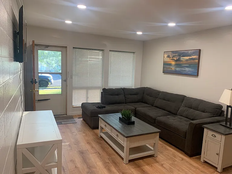 Living room includes stylish couch, console coffe table, side table, lamp, picture, television.