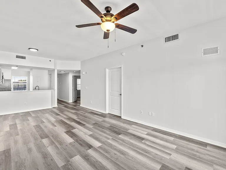 Bright, open-concept living space featuring modern hardwood flooring and elegant ceiling fan, seamlessly connected to a sleek kitchen area.