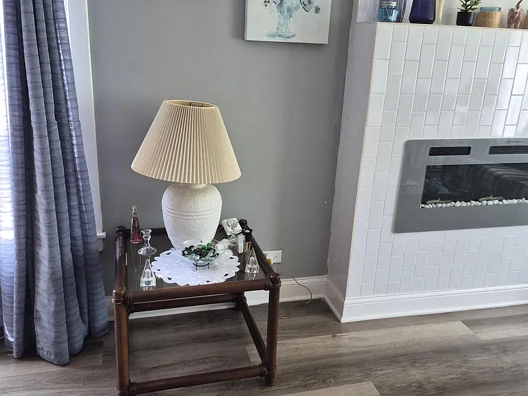 Living area with wood-look floors, window with drapes, and a tiled fireplace feature wall for relaxing.
