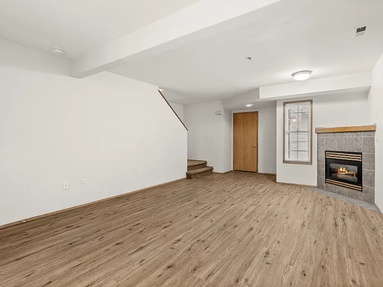 Spacious living room featuring warm wood-style floors, a cozy fireplace, and an open layout with access to the upper level. Spacious living room featuring warm wood-style floors, a cozy fireplace, and an open layout with access to the upper level.