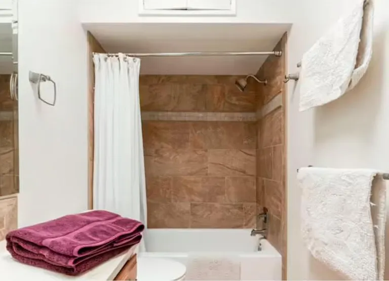 Tub and power shower with plenty of towels in the tiled bathroom