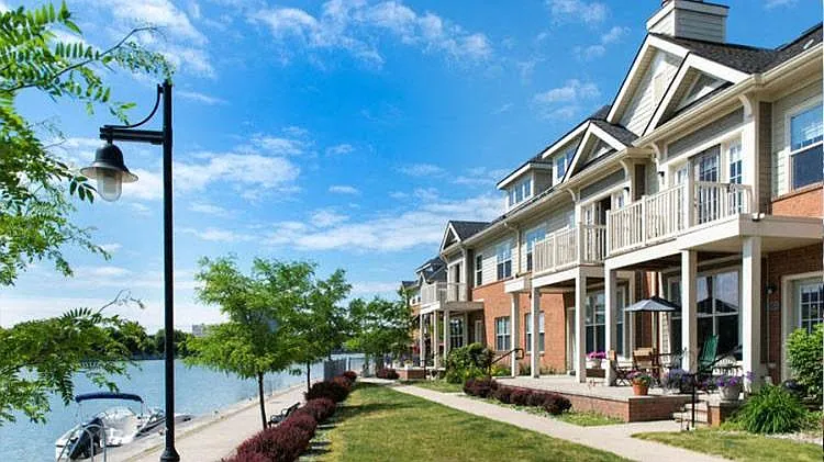 View from lawn above Genesee Riverway Trail showing private porches and balconies of apartments, sidewalks, boat mooring, and street lamps
