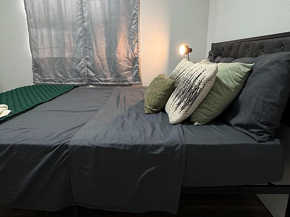 Furnished bedroom featuring a platform bed with tufted headboard, soft window treatments, and wood-look flooring.