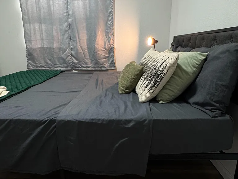 Furnished bedroom featuring a platform bed with tufted headboard, soft window treatments, and wood-look flooring.