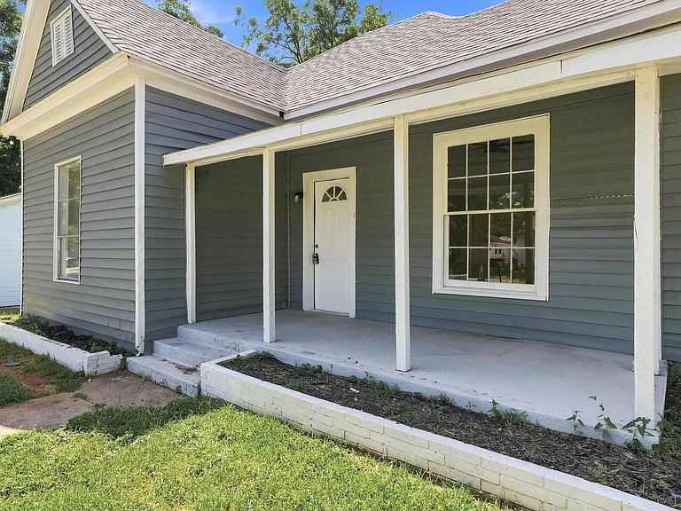 Exterior featuring horizontal siding, a covered porch with white columns, a white front door with an arched window, and a gabled architectural element