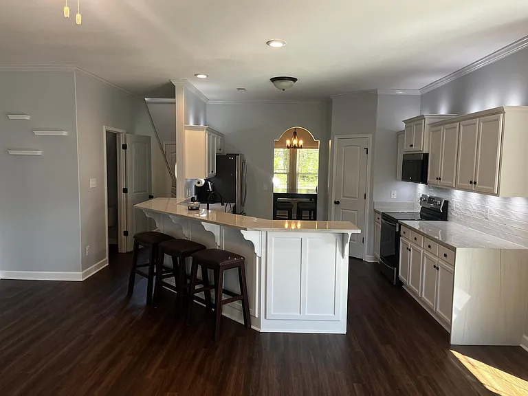 Open-concept kitchen with oversized island, three included bar stools, abundant underlit cabinetry, tiled backsplash walls, and recessed lighting.