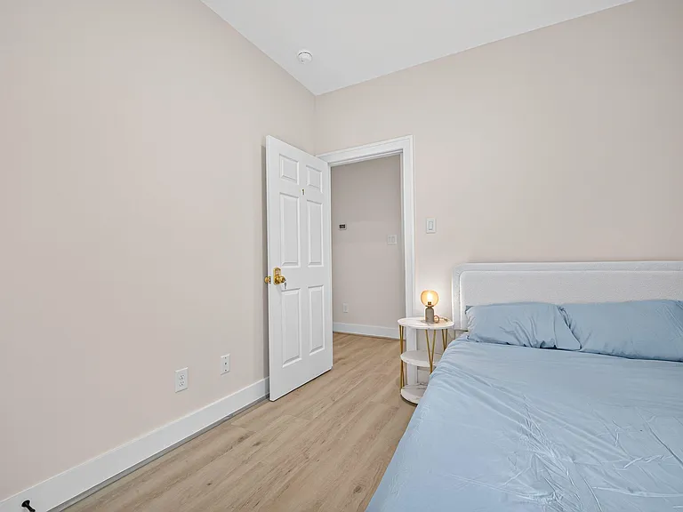 Furnished bedroom with wood-look flooring, high ceilings, and space for a full/queen bed plus a nightstand.