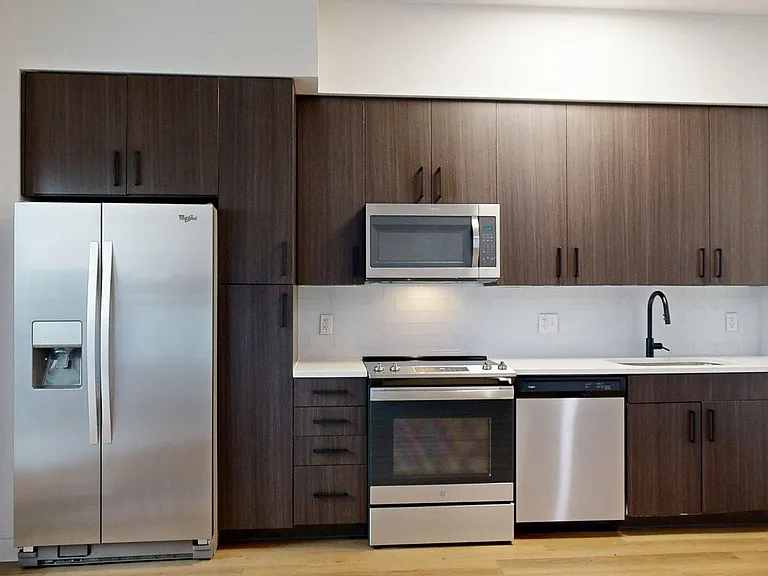 Apartment kitchen with stainless steel appliances, quartz countertops, and wood-style flooring.