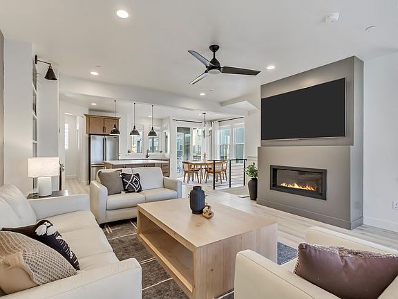 A modern living room with beige sofas and a wooden coffee table centers around the fireplace and lar