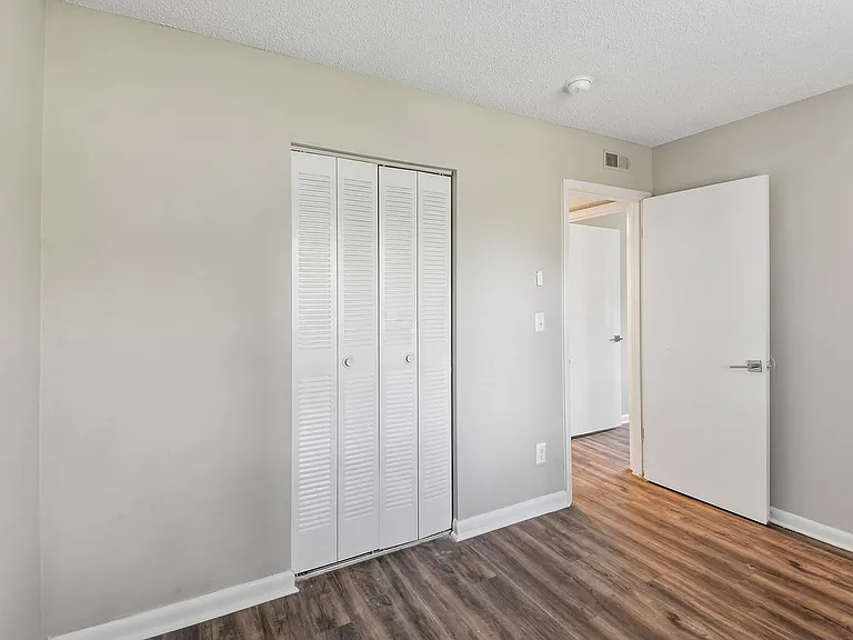Bright bedroom with stylish white closet doors and modern flooring, showcasing ample natural light and contemporary design.