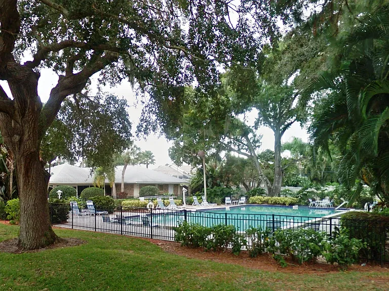 View of community large pool and club house. Gated fence surrounds pool.