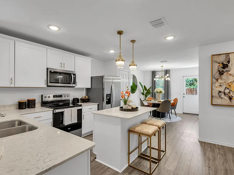 Open-concept kitchen with island seating, quartz-style counters, stainless appliances, and adjacent dining area with patio ac