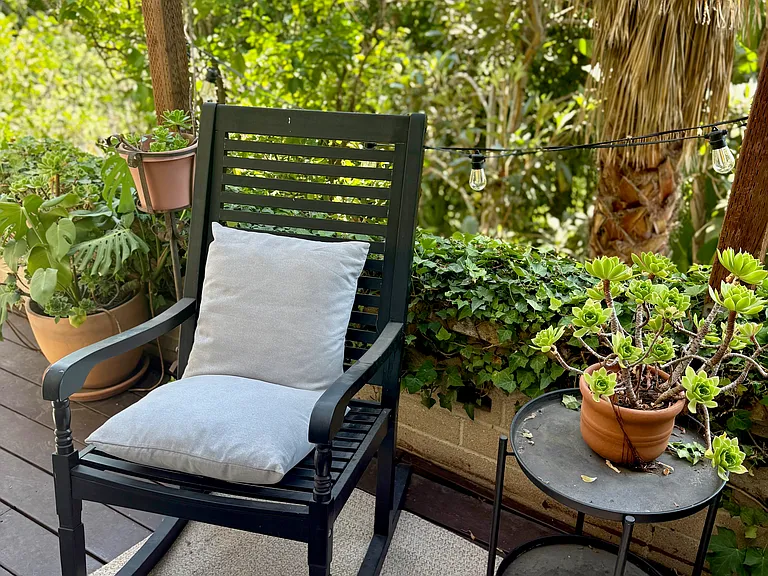 Outdoor deck furnished with a wooden rocking chair, potted succulents, and ambient lighting.