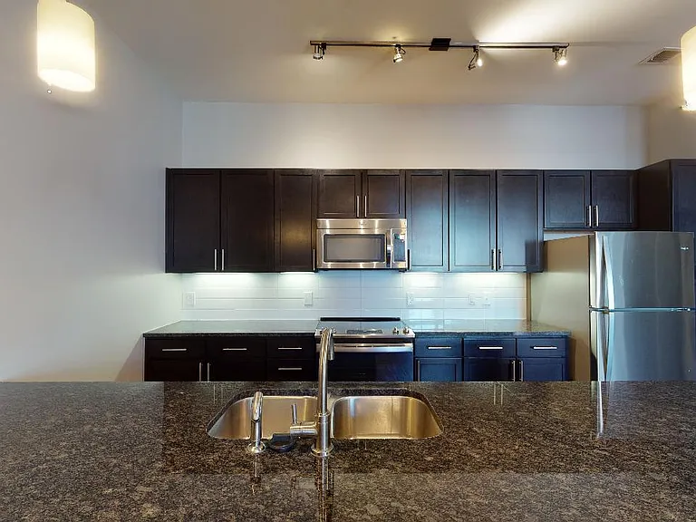 Apartment kitchen with stainless steel appliances, granite countertops and wood-style flooring.